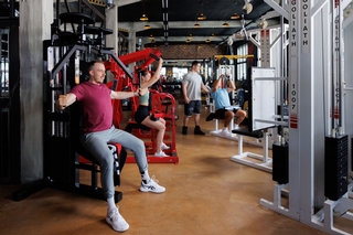Blick ins Studio während Kunden am trainieren sind und der Trainer einen Kunden bei der Ausführung korrigiert.