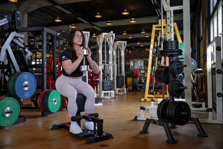 Trainerin macht Sissy Squats mit Kurzhanteln.